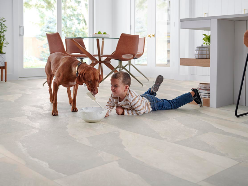 A young boy and dog make a mess on Mohawk luxury vinyl tile floors in a grey marbled pattern.